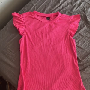 Rosa ribbad topp med volangärm Shein - Superfin rosa topp från Shein i ribbad bomullsmix. Modellen har korta volangärmar som ger en söt och trendig look. Perfekt till jeans eller kjol för en färgstark outfit. Rund halsringning och figurnära passform. Storlek: S och bör tvättas i 30 grader