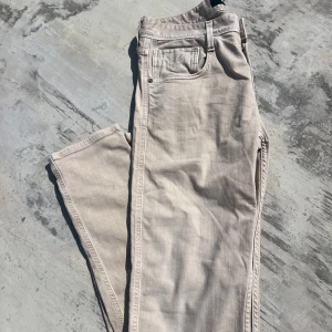 Beige Replay Anbass jeans slim fit - Snygga ljusbeige Replay Anbass jeans med klassisk femficksdesign och slim passform. Jeansen har raka ben, normal midja och är tillverkade i mjuk bomullsdenim med lite stretch för extra komfort. Perfekta för en clean och stilren look. Byxorna är i storlek W29 L32