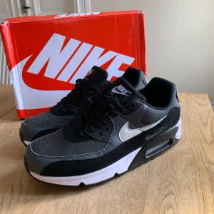 Nike Air Max 90 svart/grå/vita sneakers - Nike Air Max 90 sneakers i svart och grått med vit swoosh. Storlek 42. Dom är helt nya och oanvända, säljer pga att jag köpte fel storlek, vid frågor eller funderingar skicka ett pm, Mvh