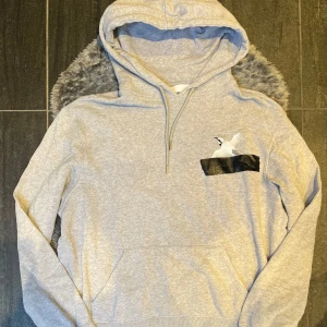 Axel Arigato Hoodie Grå - Minimalistisk och stilren hoodie från Axel Arigato i ljusgrå färg, storlek M. I mycket fint skick – mjuk, ren och utan fläckar eller hål. Perfekt för dig som gillar lyxig streetwear med diskret design.