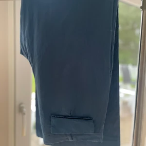 Mörkblå byxor  - Snygga mörkblå byxor med raka ben och stora framfickor. Byxorna har två bakfickor med lock och stängs med knapp och dragkedja. Perfekta för en clean och stilren look. Materialet känns lätt och passar året runt. (Oanvända. Står också strl 42 på insidan men det är mindre)