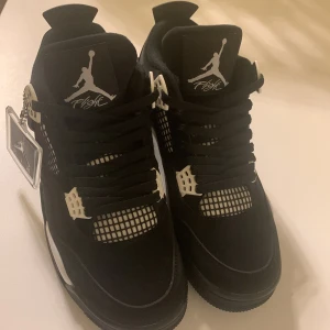 Nike Air Jordan 4 Retro svart/vit - Säljer ett par Nike Air Jordan 4 Retro i svart och vitt. Skorna har klassisk mesh på ovandelen, coola plastdetaljer och Jumpman-logga på plösen och hälen. Tjock sula och snörning ger en sportig vibe. Perfekta för dig som gillar streetwear och sneakers med attityd.