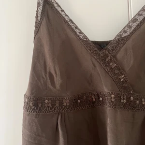 Brun y2k linnetopp med spetsdetaljer - Supersöt brun linnetopp med smala axelband och v-ringning. Toppen har fina spetsdetaljer längs urringningen och under bysten.