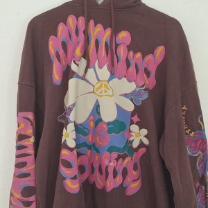 Brun hoodie med blommigt tryck Bershka - Cool brun hoodie från Bershka med färgglatt blommigt tryck och texten 'my mind is growing' i rosa, gult och lila. Tröjan har huva med snörning och långa ärmar med tryck även på ärmarna. Perfekt för dig som gillar retrovibbar och statement-plagg.