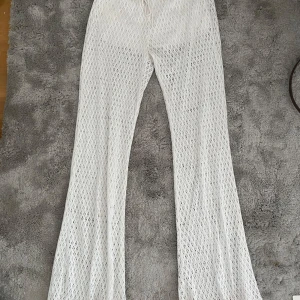 Vita spetsbyxor byxor från Bershka - Säljer ett par vita spets byxor från Bershka. Byxorna har ett luftigt, genombrutet mönster och är perfekta för sommaren. De har en relaxed fit och är riktigt snygga att styla över bikini eller med en crop top.