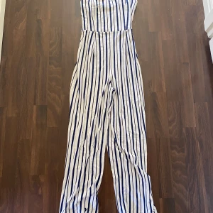 Randig byxdress från Bershka S - Snygg byxdress från Bershka i vitt med marinblå vertikala ränder. Ett litet hål vid ena benet men annars hel. 