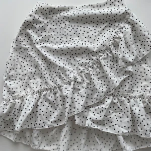 Prickig volangkjol från SHEIN XS - Supersöt vit kortkjol från SHEIN med svarta prickar och volangdetaljer. Kjolen har omlottkänsla och dragkedja i sidan. 