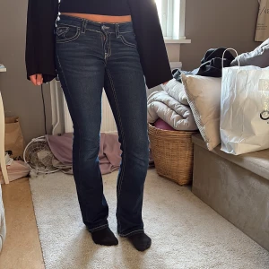 Mörkblå bootcut jeans med kontrastsömmar - Snygga mörkblå jeans med bootcut passform och markerade vita kontrastsömmar. Klassisk femficksmodell med coola detaljer på bakfickorna. Jeansen har normal midja och är tillverkade i stretchig denim för en bekväm känsla.
