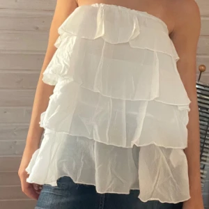 Vit volangig topp - Supersöt vit bandeau tubtopp från Heartquake med flera lager volanger. Toppens tyg är lätt och luftigt, perfekt för varma dagar. Den är axelbandslös och har en flowy känsla som ger en riktigt somrig vibe.💓🫶