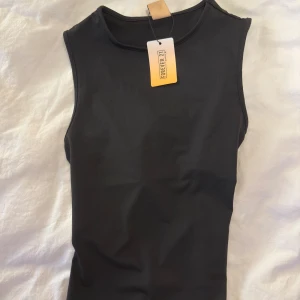 Svart ärmlös topp från Forever 21 - Svart ärmlös topp från Forever 21 med rund halsringning och snygg snörningsdetalj i sidan. Toppens material är stretchigt och känns mjukt mot huden, perfekt för en clean och stilren look. Passformen är normal och toppen är enkel att matcha med olika outfits.