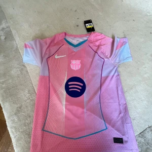 FC Barcelona Lamine Yamal rosa tröja Nike - Säljer en FC Barcelona fotbollströja med Lamine Yamal och nummer 10 på ryggen. Tröjan är rosa med ljusblå och vita detaljer, har korta ärmar.