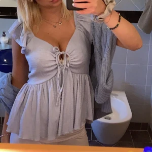 Ljusblå volangblus från 157 - Supersöt ljusblå blus från 157 med volangärmar och knytning framtill. Toppen har en luftig, flowy passform och är tillverkad i ett lätt, krinklat tyg som ger en chill vibe. Perfekt för varma dagar och snygg till både jeans och kjol.