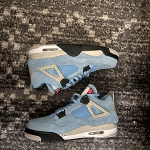 J4 University Blue - Nike Jordan 4 University Blue sneakers med ljusblå mocka, meshpaneler och detaljer i grått med svarta och vita inslag. Snygga speckled detaljer på mellansulan och klassisk Jumpman-logga under sulan. Skorna har snörning och en chunky siluett som sticker ut.