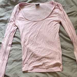 Ljusrosa långärmad topp Gina Tricot - Supersöt ljusrosa långärmad topp från Gina Tricot i mjuk bomull. Djup rundad urringning och liten slits vid ärmslutet ger en extra touch. Perfekt att styla med jeans eller kjol för en chill look.