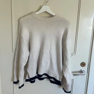 Beige stickad tröja från Gina Tricot - Beige stickad tröja från Gina Tricot med svarta detaljer vid ärmslut och nederkant. Vidare ärmar. Använd några gånger men i fint skick 