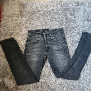 Grå slim fit jeans från Jack & Jones - Snygga svarta/gråa jeans från Jack & Jones med slim fit och klassisk femficksdesign. Jeansen har en tvättad look med ljusare partier och svarta detaljer vid midjan. Perfekta för dig som gillar en smal siluett och streetinspirerad stil.