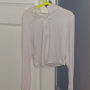 Ljusrosa/krämvit croppad hoodie med half zip - Säljer en ljusrosa/ krämvit croppad tränings jacka med huva och half zip framtill. Tröjan har långa ärmar och är gjord i ett mjukt, syntetiskt material som känns skönt mot huden. Perfekt för dig som gillar en clean och enkel stil med lite sportig vibe. 