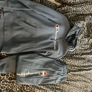 Blå Champion hoodie med logga och matchande mjukis  - Snygg blå hoodie från Champion med stor broderad logga och huva. Tröjan har känguruficka framtill och långa ärmar. Perfekt för en chill och sportig stil. Passar dig som gillar streetwear och vill ha något bekvämt och trendigt.