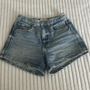Blå jeansshorts från Zara - Snygga blå jeansshorts från Zara med klassisk femficksdesign och knappstängning. Shortsen har en loose passform och är tillverkade i slitstarkt denim med ljus tvätt. Perfekta för chill dagar och sommarhäng. Elastisk midja baktill för extra komfort.