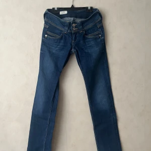 Blå jeans - Snygga blå jeans från Pepe Jeans med raka ben och låg midja. Jeansen har dubbla knappar i midjan, klassiska fickor fram och bak samt kontrastsömmar. Materialet är jeans med en cool tvätt och Pepe Jeans-logga på bakfickan. Super skick.