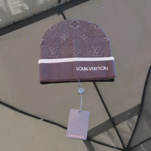 Louise vuitton mössa - Snygg svart mössa med klassiskt monogrammönster och vit rand runt kanten. Mössan har broderad text framtill och är stickad i mjukt material. Perfekt för dig som gillar exklusiva accessoarer och vill sticka ut.