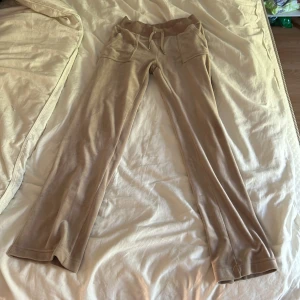 Beige mjukisbyxor Juicy Couture XS - Snygga beige mjukisbyxor från Juicy Couture i storlek XS. Byxorna har bootcut-ben, bred resår i midjan med snörning och stora fickor fram och bak. Mjukt och skönt material . Smått knottrig i midjan 