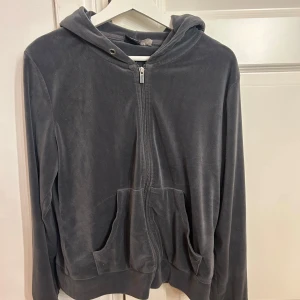 Mörkgrå hoodie från Gina Tricot - Mjuk och skön mörkgrå hoodie från Gina Tricot i storlek L. Tröjan har huva, dragkedja framtill och två stora fickor. Materialet är lent och har en lätt glansig finish, perfekt för chill dagar. Långärmad och loose passform för extra comfort.