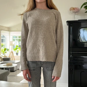 Beige stickad tröja med ribbade muddar - Mysig beige stickad tröja med rund hals och långa ärmar. Tröjan har ribbade muddar vid ärmslut och nederkant, vilket ger en chill och enkel look. Perfekt för lager-på-lager och passar till jeans eller mjukisbyxor. Materialet är mjukt och känns skönt mot huden.
