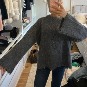 Grå fluffig stickad tröja Stockh LM - Supermysig grå stickad tröja från Stockh LM Studio i storlek S. Tröjan har en fluffig och lite ruffig yta, breda långa ärmar och rund hals. Perfekt för hösten och lite svalare kvällar. 