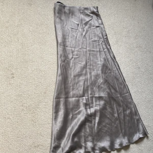 Satinlångkjol XS från Black Label - Två stilrena långkjolar i satin från The Black Label Collection, storlek XS. Ena kjolen är pärlfärg och den andra är svart, båda har en mjuk, glansig finish och bred elastisk midja. Perfekt för dig som gillar minimalistisk och elegant vibe. OM DU KÖPER 1 SÅ KOSTAR DE 150kr men om du köper två blir de 250kr!