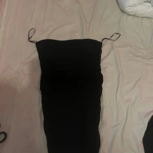 Svart omlottklänning från Zara - Säljer en svart kort klänning från Zara med smala axelband och snygga rynkade detaljer längs sidorna. Klänningen har omlott-design och är figurnära, perfekt för dig som gillar en stilren och trendig look. Materialet är mjukt och stretchigt för skön passform.