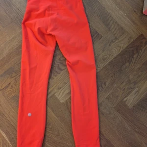 Röda leggings från Lululemon - Snygga röda leggings från Lululemon med hög midja och tight passform. Tillverkade i ett stretchigt material med 77% nylon och 23% lycra för maximal komfort. Perfekta för träning eller chill dagar. Diskret Lululemon-logga på benet. Matchar perfekt med tröjan nedanför! Beredd att gå ner i pris vid snabb affär.