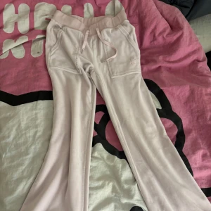 Ljusrosa mjukisbyxor Juicy Couture XXS - Säljer ett par ljusrosa mjukisbyxor från Juicy Couture i storlek XXS. Byxorna har bootcut-ben, snörning i midjan och fickor både fram och bak med knappdetaljer. Mjukt material som känns skönt mot huden och klassisk Juicy Couture-logga på fickan. Andvänt ett par gånger men den har inga skador och ser normal ut!