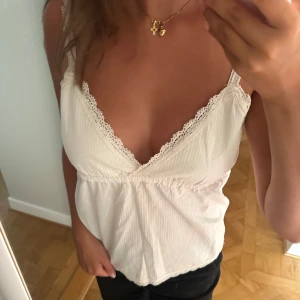 Vit spetsdetaljerad linnetopp Brandy Melville - Supersöt vit linnetopp från Brandy Melville med tunna axelband och v-ringning. Toppen har diskreta ränder och fina spetsdetaljer längs urringning och nederkant. 