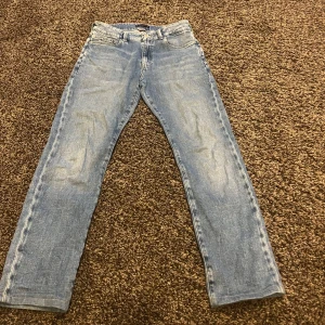 Ljusblå jeans från Tommy Hilfiger - Säljer ett par klassiska ljusblå jeans från Tommy Hilfiger. Jeansen har fem fickor, snyggt läderpatch bak och diskret logga på bakfickan. 