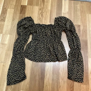Leopardmönstrad blus med puffärm - Säljer en snygg blus med leopardmönster i svart och beige. Blusen har puffiga långa ärmar, smockad midja och axlar samt en luftig passform nedtill. Perfekt för dig som vill sticka ut med coola detaljer och trendigt mönster.