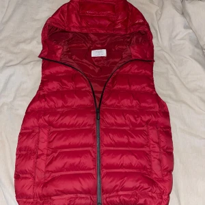 Röd dunväst med huva - Röd dunväst från Zara med huva och dragkedja framtill. Västen är vadderad och har en sportig look, perfekt för lager-på-lager-stil. Passar dig som gillar färg och vill hålla värmen utan att tumma på stilen.