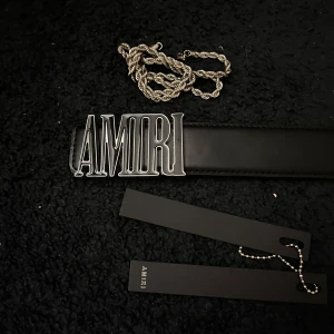 Svart bälte med stor AMIRI-logga halsband och taggen ingår - ! Hör av dig innan du köper! Säljer ett svart bälte från AMIRI med en stor, blank metallspänne där det står AMIRI. Bältet är stilrent och har en klassisk form med tydlig logotyp framtill. Perfekt för dig som vill ha en statement-accessoar.