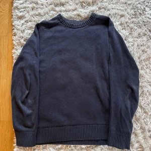 Mörkblå stickad tröja från Riley  - En enkel och stilren mörkblå stickad tröja med rund halsringning och ribbade muddar vid ärmslut och nederkant. Perfekt för lager-på-lager och passar till det mesta.