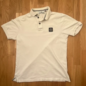 Vit piké från Stone Island - Vit pikétröja från Stone Island med svart logotyp-patch på bröstet. Size S för män