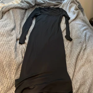 Svart långklänning från Gina Tricot - En stilren svart långklänning från Gina Tricot med lång ärm och rund halsringning. Klänningen har en figurnära passform och är tillverkad i ett mjukt, stretchigt material som ger en elegant siluett.