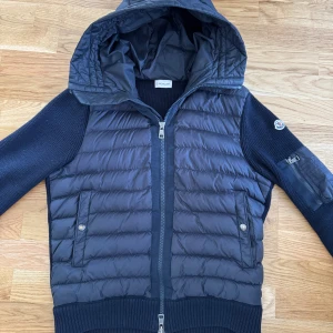 Mörkblå pufferjacka med huva från Moncler - Tja nu säljer vi denna moncler cardigan i mörkblå färg med luva och en klassisk moncler logga på armen och är i ett gott skick (9/10 den är i storlek M och passar den som är runt 180 lång, hör av er till oss vid fundering, möts i kungälv eller stenungsund eller fraktar med spårbart paket via postnord