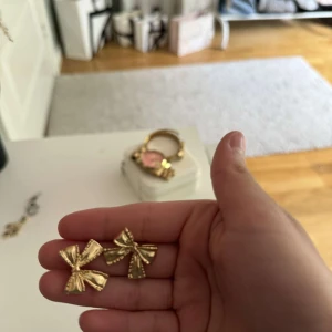 Guldiga rosettörhängen - ”PLOPPARNA ÄR BORTA”Säljer ett par fina örhängen i form av rosetter i guldig färg. Perfekta för att ge en söt och trendig touch till din outfit. Passar dig som gillar accessoarer med det lilla extra.
