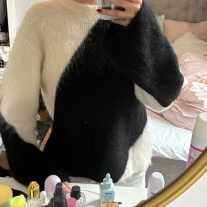 Svartvit stickad tröja - Säljer en fluffig och mysig stickad tröja i svart och vitt. Tröjan har lång ärm och en cool diagonal färgdelning som ger en unik look. Perfekt för dig som gillar att sticka ut lite extra!