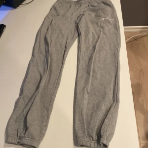 Grå mjukisbyxor från Champion - Säljer ett par grå mjukisbyxor från Champion Kid Collection i storlek L (150/155 cm). Byxorna har resår i midjan och vid bensluten samt en vit Champion-logga på ena benet. Perfekta för chill eller träning.