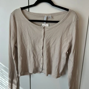 Beige ribbad croppad top - Säljer en beige croppad top från H&M Divided med ribbad struktur och knappar framtill. Tröjan har lång ärm och en rundad halsringning. 