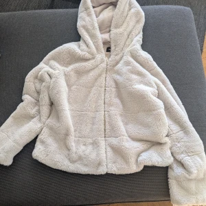 Ljusbeige teddyjacka med huva - Mysig och fluffig teddyjacka i ljusbeige färg med huva och dragkedja framtill. 