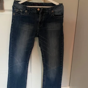 Mörkblå jeansbyxor med raka ben - Säljer ett par mörkblå jeansbyxor med klassisk femficksdesign och raka ben. Jeansen har diskreta slitningar framtill och stängs med dragkedja och knapp. Perfekta för en avslappnad stil.