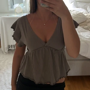 Blus med knyt i ryggen - Säljer denna fina grå/bruna blus med v-ringning, volangärmar och knytning i ryggen. 