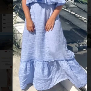 Ljusblå långklänning i linne från Vesna W - Superfin ljusblå långklänning i linne med volangdetalj nertill. Perfekt för varma dagar och har en avslappnad passform. Klänningen har en enkel och stilren design som passar till många tillfällen.